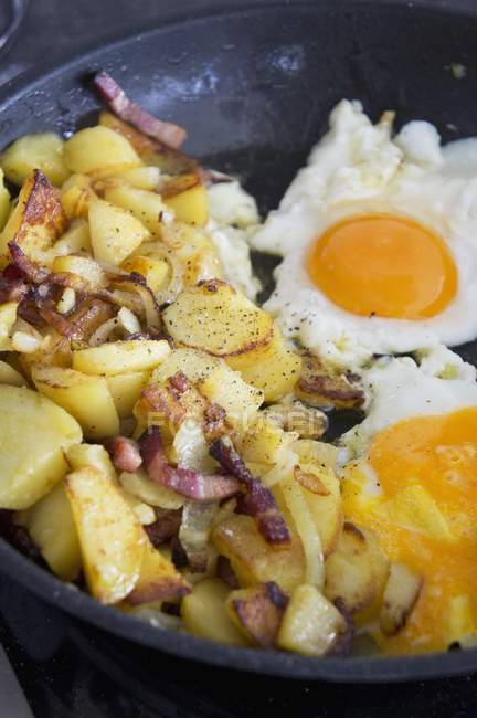 Смажена картопля з беконом і смаженими яйцями на сковороді — стокове фото