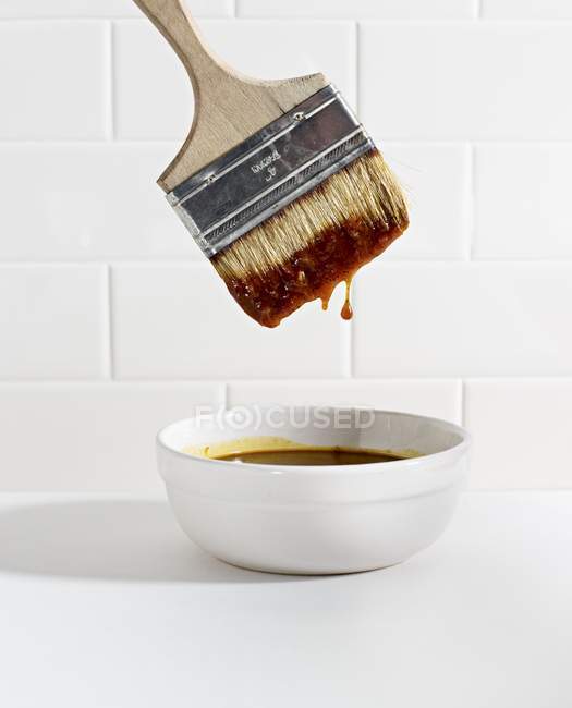 Vista de primer plano de un cepillo sumergido en un tazón de salsa barbacoa - foto de stock