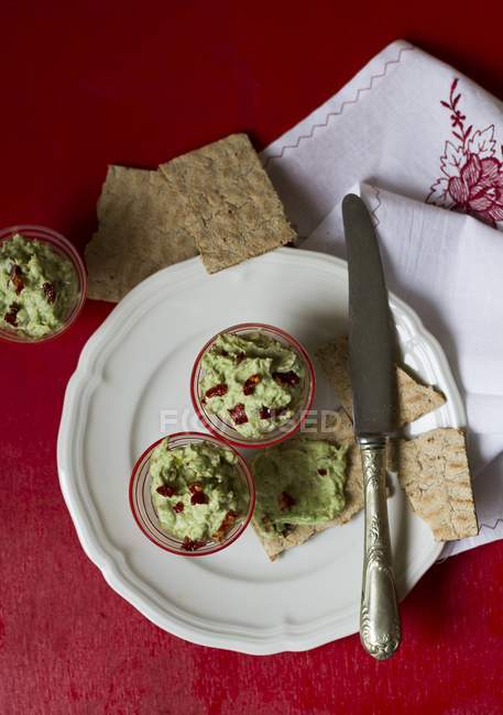Avocado cream with dried tomatoes on white plate with knife — Stock Photo
