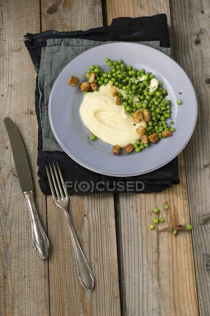 Mashed potatoes with buttered peas and diced tofu on grey plate over wooden surface with fork and knife — Stock Photo