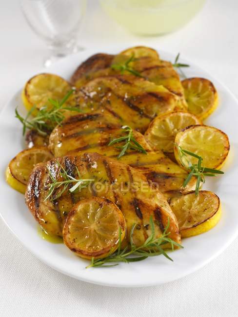 Closeup view of grilled chicken in sauce garnished with lemon and rosemary on a platter — Stock Photo