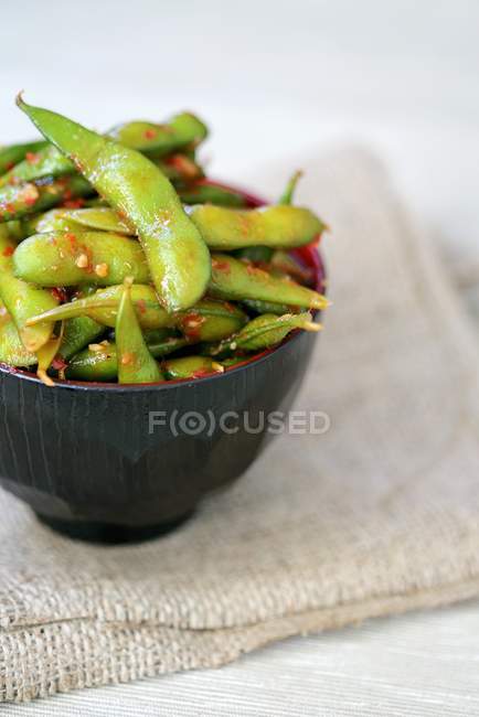Soya beans in a spicy chilli sauce in black bowl over towel — Stock Photo