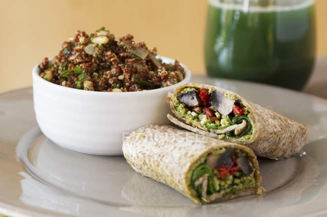 Wholemeal wraps filled with portobello mushrooms, pesto, dried tomatoes and courgettes next to a bowl of quinoa with cabbage and coconut milk — Stock Photo