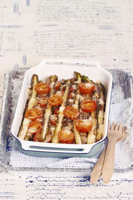 Espargos gratinados com tomates em prato branco sobre toalha com garfos de madeira — Fotografia de Stock