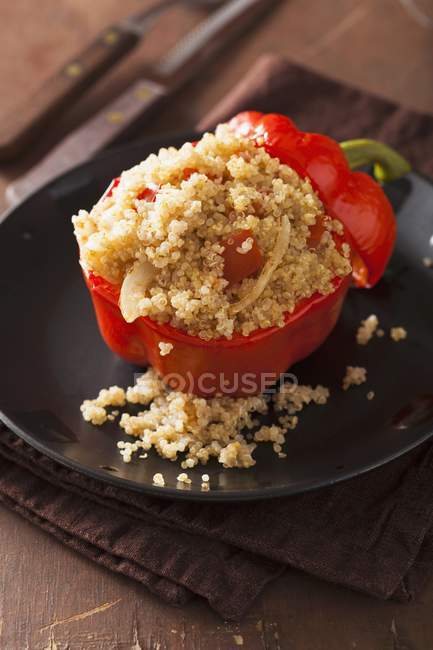 Un poivron rouge rempli de quinoa sur une assiette noire sur une serviette — Photo de stock