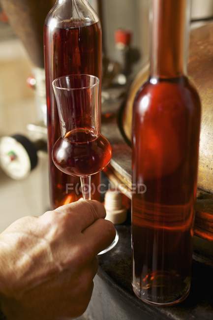 Nahaufnahme einer Hand mit einem Glas Zirbenschnaps in der Nähe von Flaschen — Stockfoto