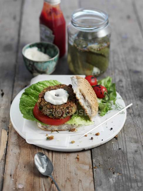 Ein Kichererbsen-Burger mit Joghurt und Gurken auf weißem Teller über der Holzoberfläche — Stockfoto