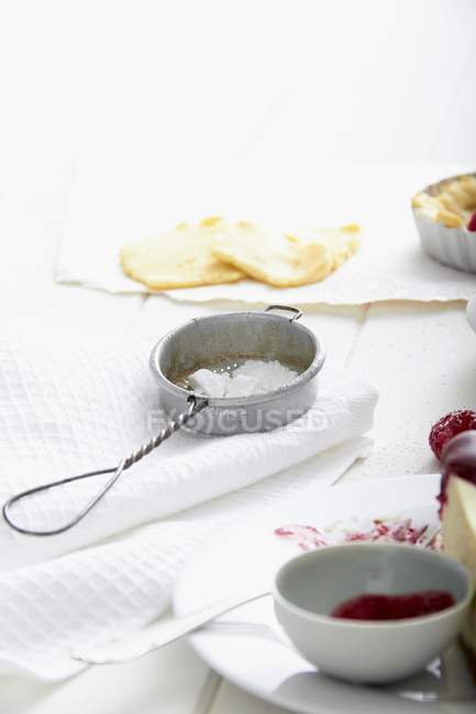 Closeup view of arrangement of raw shortcrust pastry and icing sugar in a sieve — Stock Photo