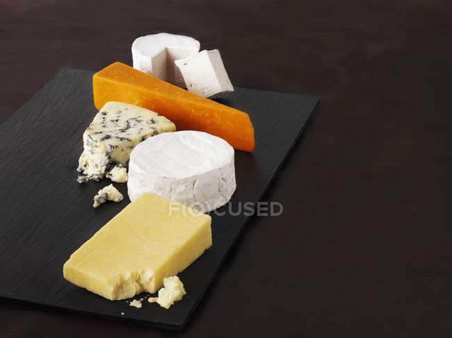 Selection of cheeses on black platter — Stock Photo