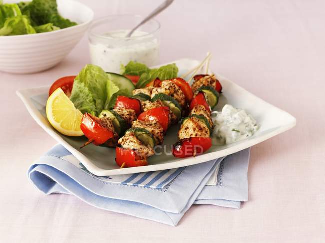 Greek chicken, pepper and courgette kebabs with salad  on white plate over towel — Stock Photo