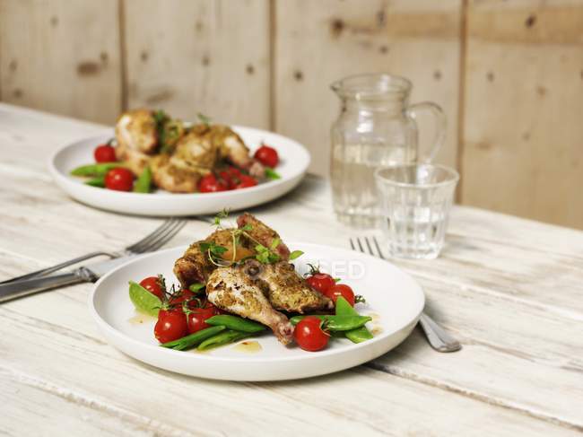 Half a herb chicken with tomatoes and mange tout on white plates over wooden surface — Stock Photo