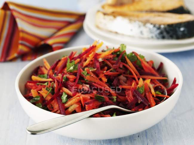 Красочный морковный салат с петрушкой на белой тарелке с ложкой — стоковое фото