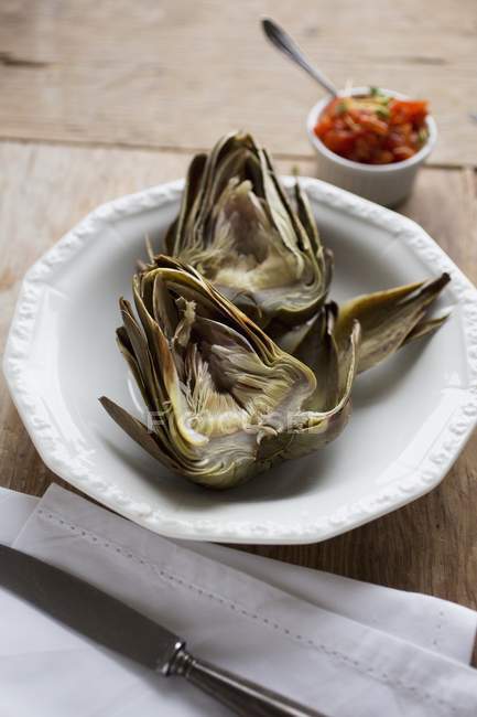 A boiled artichoke with tomato salsa and on white plate over wooden surface — Stock Photo