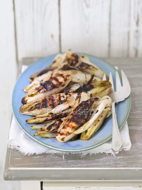 Grilled chicory with balsamic vinegar on blue plate over grey wooden surface — Stock Photo