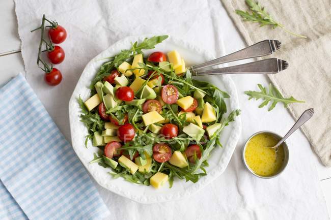 Insalata di avocado e mango con rucola e pomodorini in piatto bianco su stoffa — Foto stock