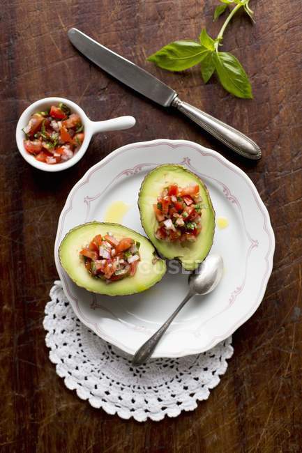 Stuffed avocado with tomato salsa on white plate with spoon over wooden surface — Stock Photo