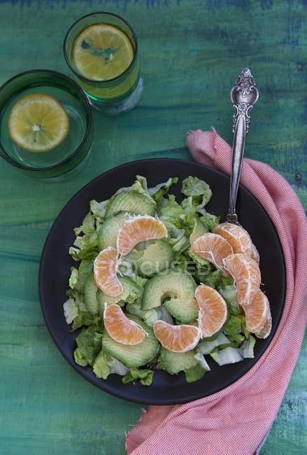 A mixed leaf salad with avocado and clementines on green wooden surface — Stock Photo
