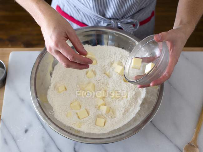 Person fügt gewürfelte Butter zum Mehl in Edelstahlschüssel hinzu — Stockfoto