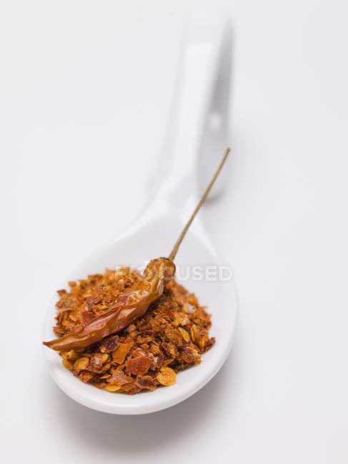 Fiocchi di peperoncino e peperoncino essiccato su cucchiaio su superficie bianca — Foto stock
