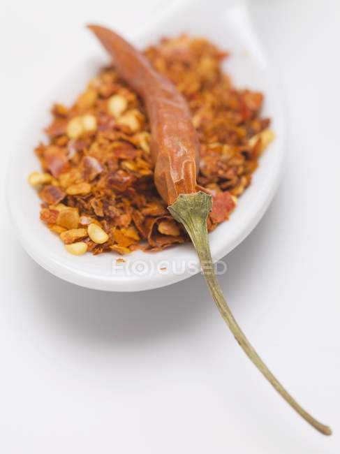 Flocos de pimenta e pimenta seca na colher no fundo branco — Fotografia de Stock