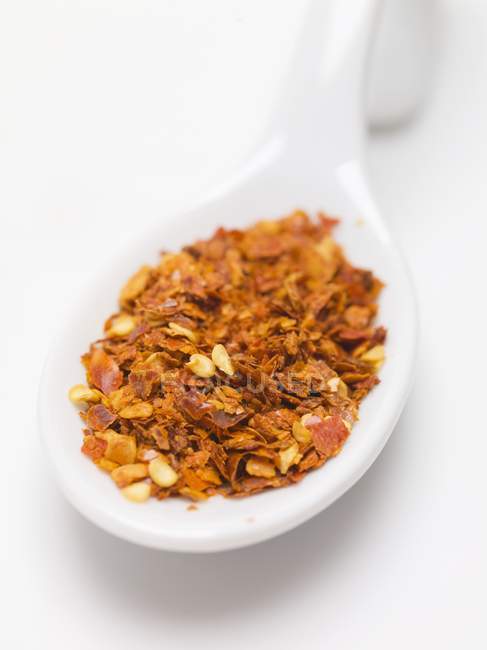 Chilli flakes on spoon over white surface — Stock Photo