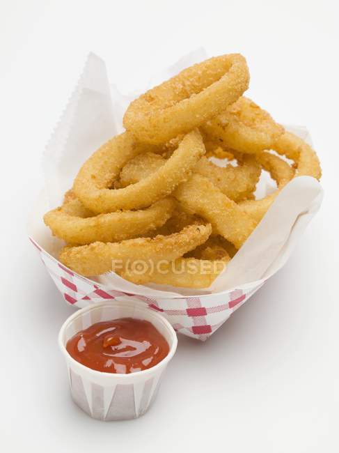 Луковые кольца с кетчупом в бумажной тарелке — стоковое фото