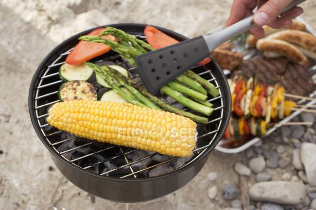 Hand turning asparagus on barbecue with barbecue tongs — Stock Photo