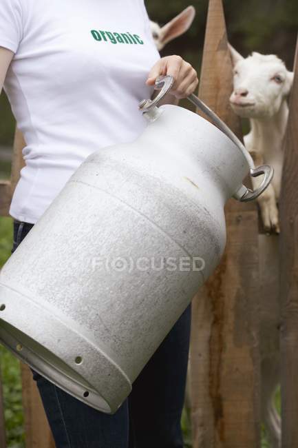 Vista diurna ritagliata di donna con lattina di latte di fronte alla stalla di capra — Foto stock