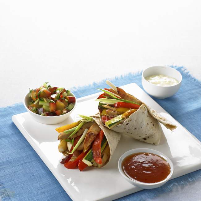 Fajitas de pollo y verduras con salsa de ciruela picante en plato blanco sobre toalla azul - foto de stock