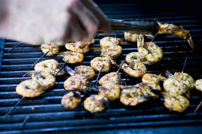 Closeup cropped view of hand arranging prawn skewers on barbecue rack — Stock Photo