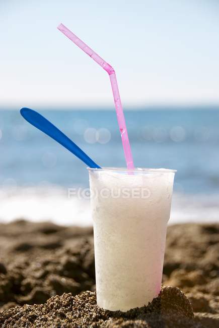 Крупный план Граниты в стакане с соломой и ложкой на песчаном пляже — стоковое фото