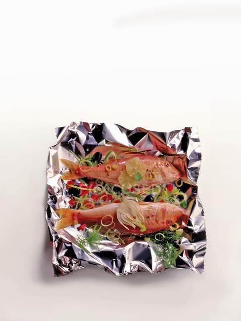 Salmonete rojo con verduras y hierbas sobre papel de aluminio sobre superficie blanca - foto de stock