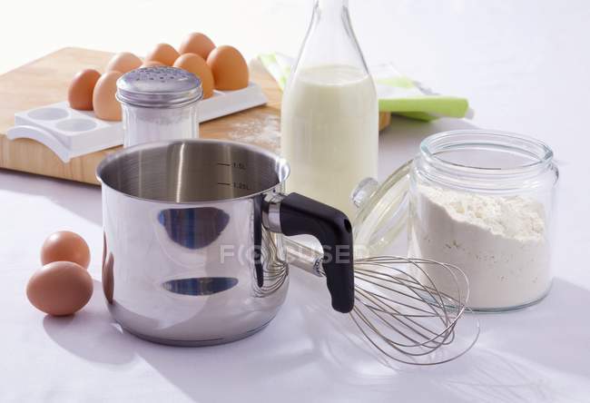 Elevated view of still life with eggs, flour, milk, pan and whisk — Stock Photo