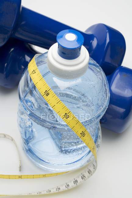 Vue rapprochée de la bouteille d'eau avec ruban à mesurer et haltères — Photo de stock