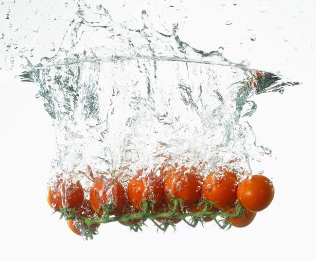 Cherry tomatoes falling into water — Stock Photo