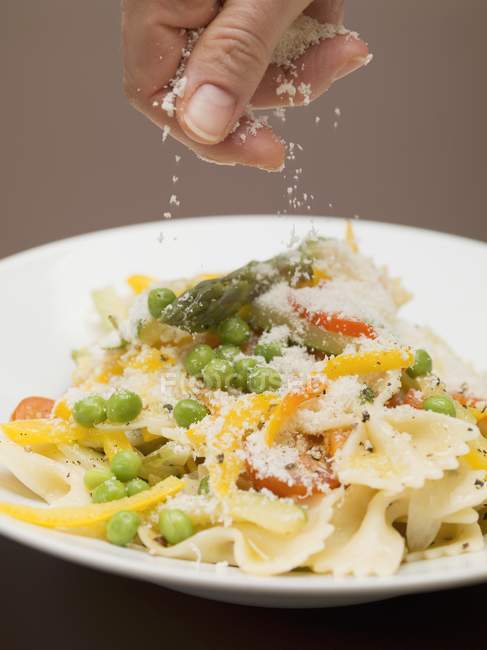 Hand sprinkling cheese on farfalle pasta — Stock Photo