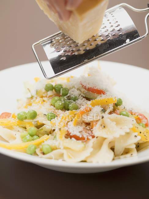 Hand grating Parmesan onto farfalle pasta — Stock Photo