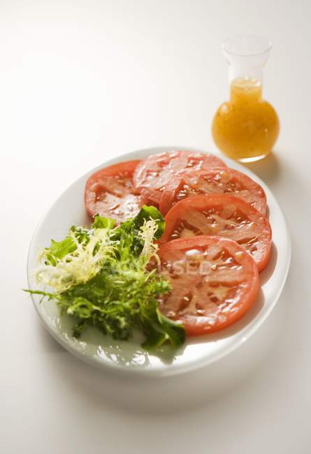 Tomates em fatias com verdes; Molho de salada em prato branco — Fotografia de Stock
