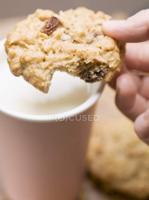 Closeup view of hand holding cookie over a beaker of milk — Stock Photo