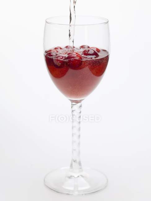Closeup view of water flowing to cranberry drink in glass — Stock Photo