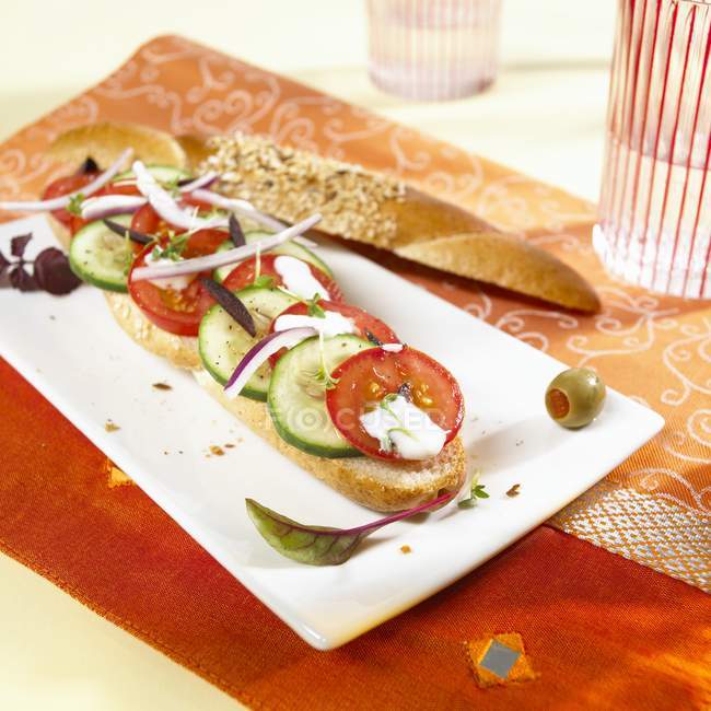 A grain baguette topped with Greek salad on white plate — Stock Photo