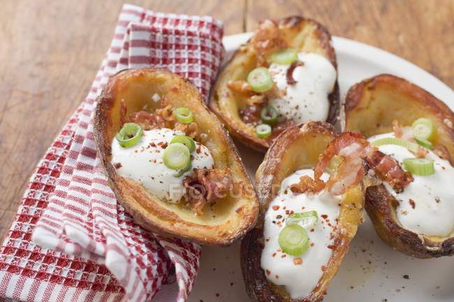 Baked potato skins with bacon and sour cream  over wooden surface with towel — Stock Photo