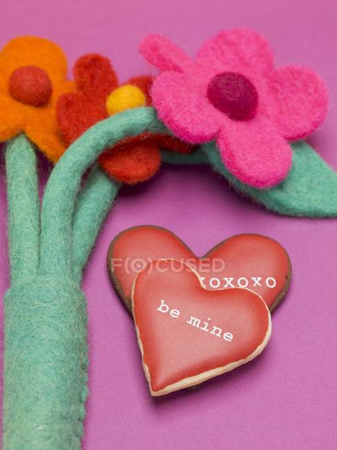 Closeup view of heart-shaped biscuits with red icing and felt flowers — Stock Photo