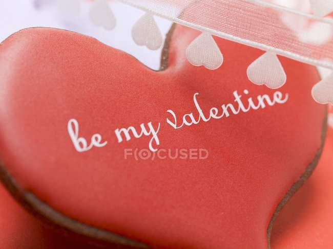 Vista de cerca de la galleta de chocolate en forma de corazón con glaseado rojo y escritura - foto de stock