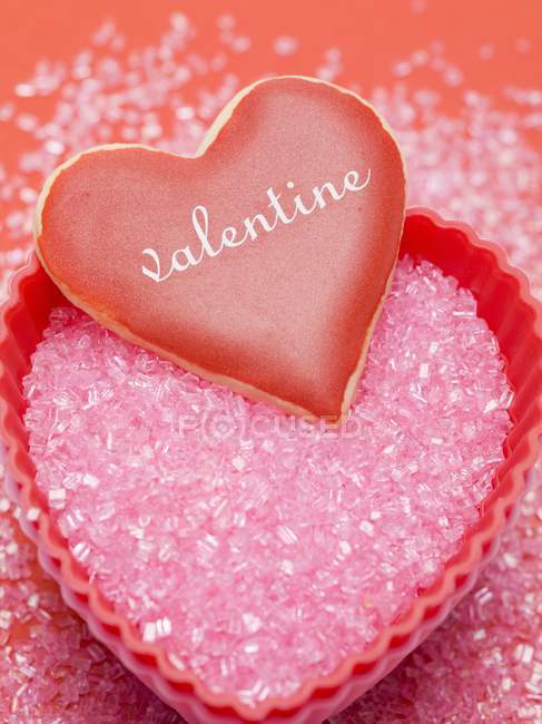 Closeup view of vanilla heart with red icing on pink sugar — Stock Photo
