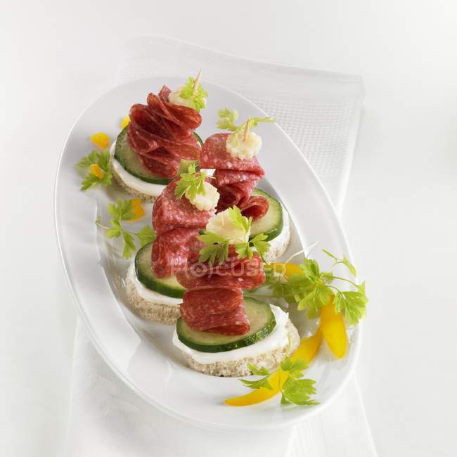 Salame e canapè di cetriolo su piatto bianco sopra asciugamano — Foto stock