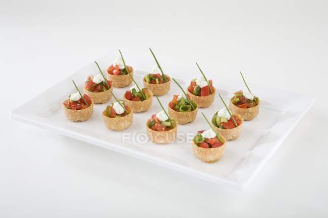 Croustades con cebolletas, tomates cherry, salsa de ajo en el plato sobre fondo blanco - foto de stock