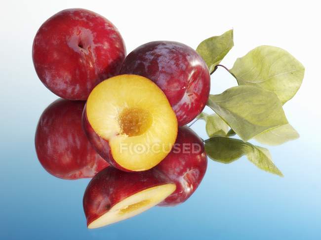 Prunes rouges avec moitié et feuilles — Photo de stock