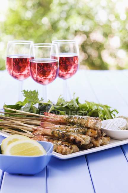 Шашлыки с креветками на гриле с чесночным маслом и бокалы с красным вином на открытом воздухе — стоковое фото