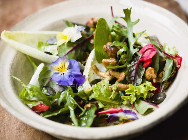 Lechuga mixta con flores comestibles y champiñones chanterelle en plato blanco - foto de stock
